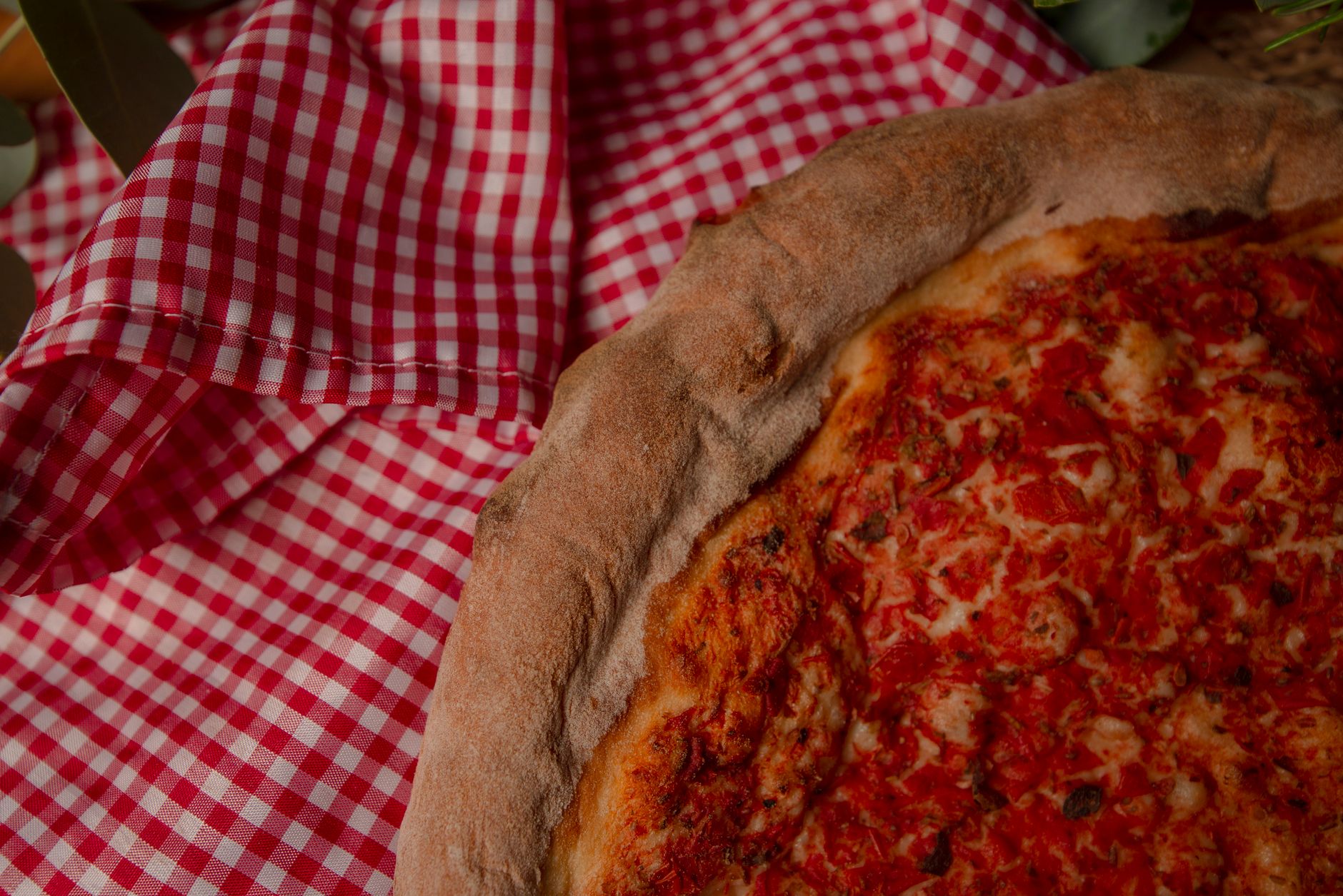Close-up of a thick-crust pizza slice next to a red checkered cloth