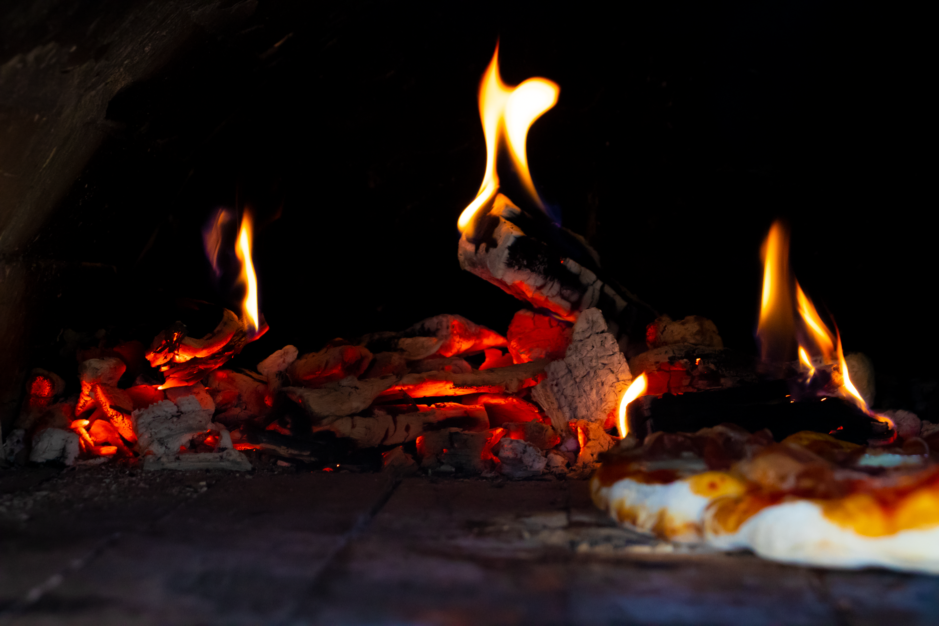 Close-up of a stone oven with bright flames baking a pizza