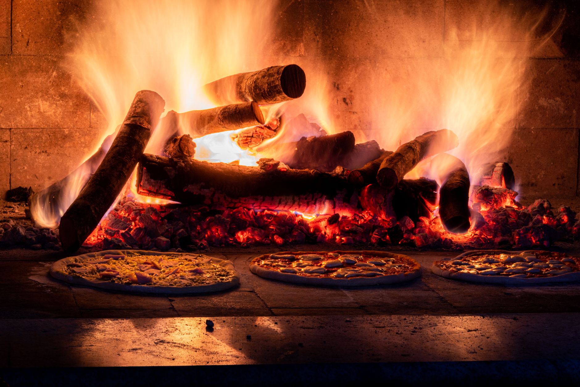 Pizza baking in a rustic wood-fired oven with visible flames
