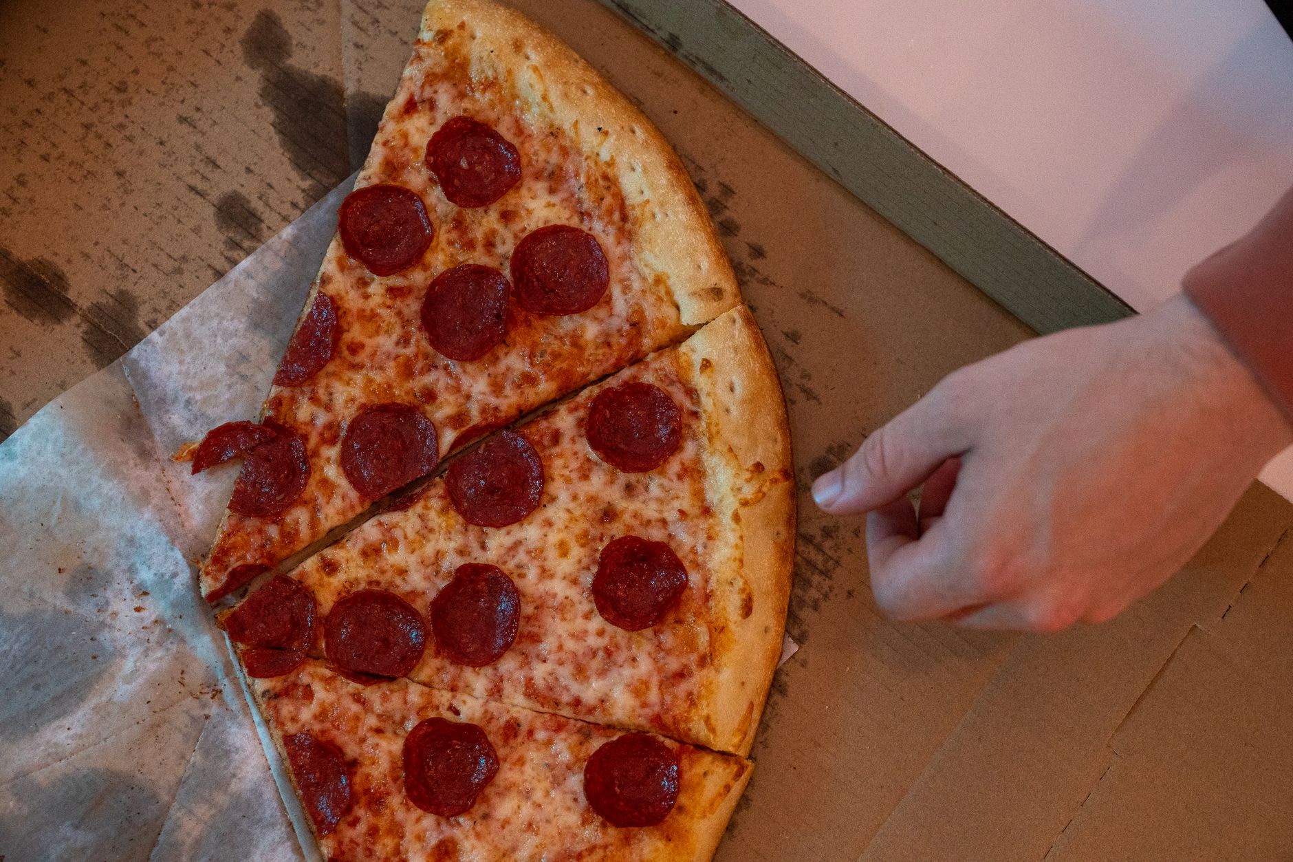 Pepperoni pizza slice lifted from a cardboard takeout box