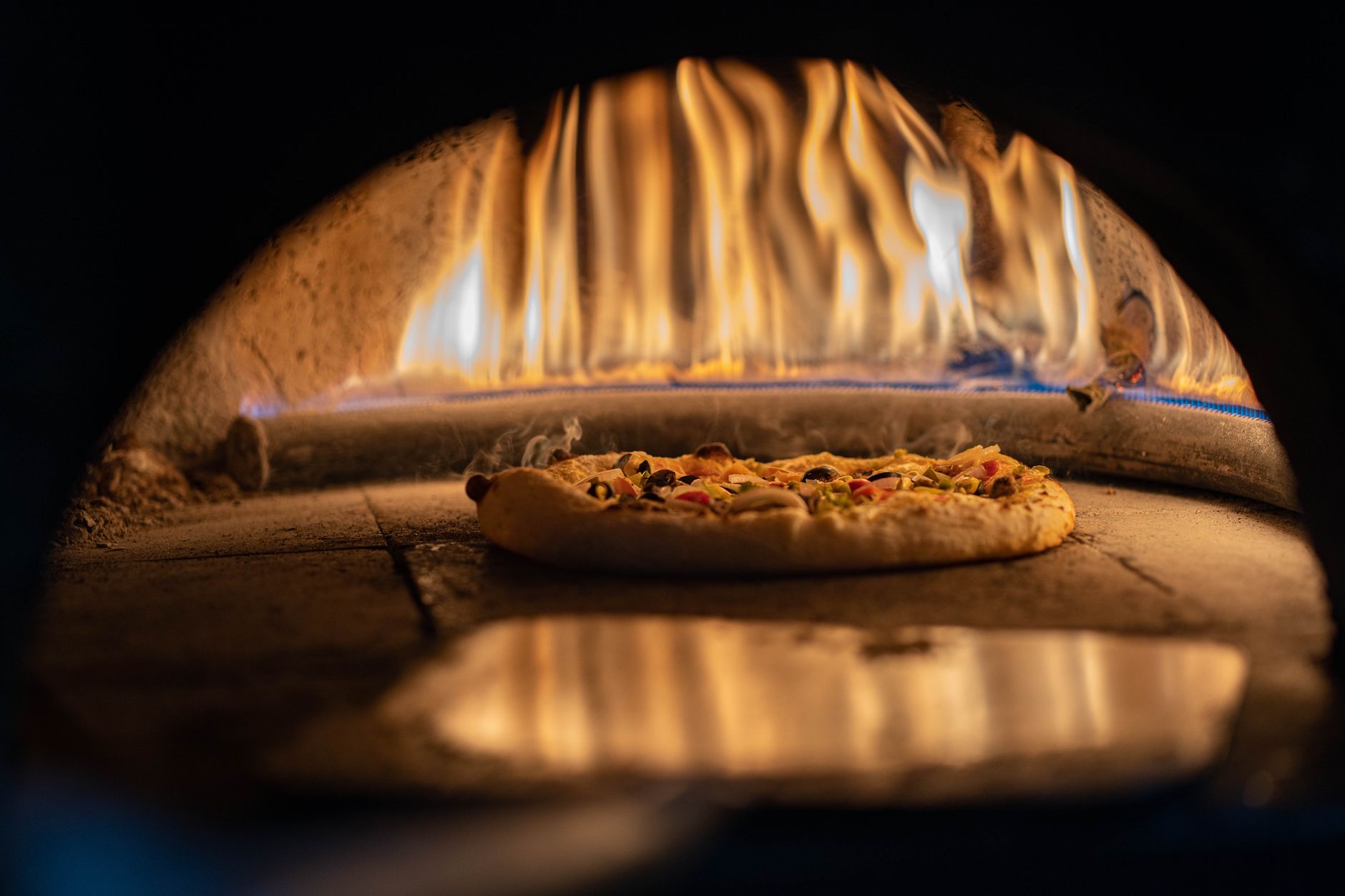 Pizza baking in a traditional wood-fired oven with vibrant flames