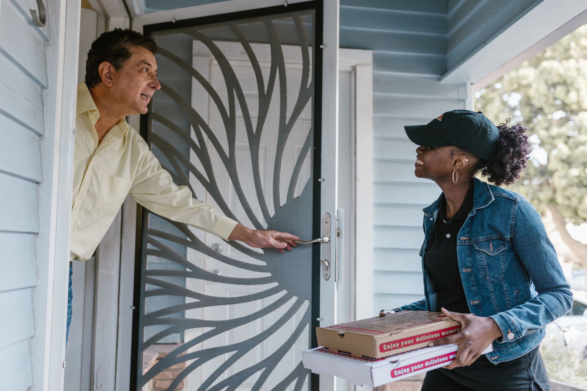 Delivery driver handing pizza boxes to a customer at the front door