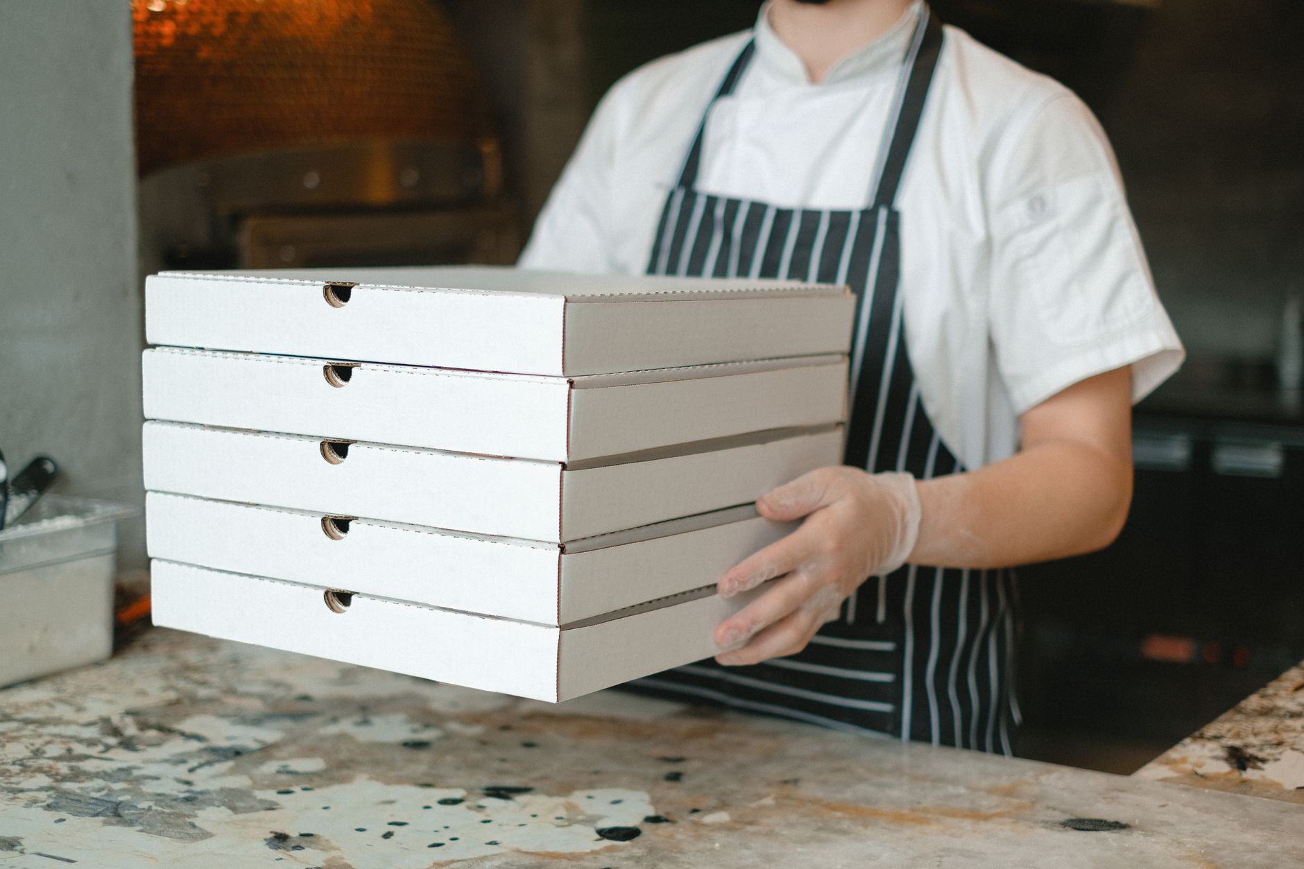 Stacked pizza delivery boxes being carried in a kitchen